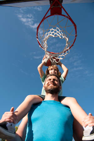 Father and son playing basketball. Father carrying his son on shoulders on the basketball court.