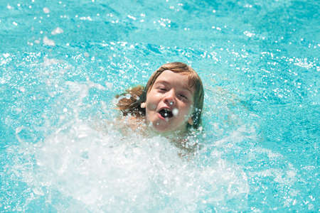 Child boy swim in swimming pool. Splash water. Little boy playing in outdoor swimming pool in water on summer vacation. Child learning to swim in outdoor pool.の写真素材