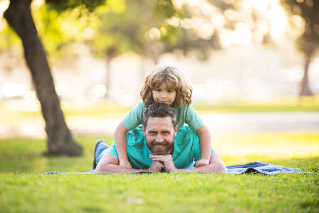 Dad with cute child boy laying on grass in summer park outdoor. Father and son relaxing on nature.の写真素材