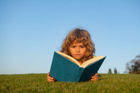 Child boy with a book in the garden. Kids success, successful leader concept. Kid is readding a book playing outdoors in summer day.の写真素材