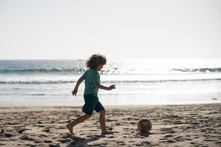 Little boy child play football on coast of sea beach. Summer kids sports.の写真素材