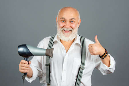 Senior hairdresser or barber with happy emotional face in studio on grey background. Man with Blow-dry with thumb up.の写真素材