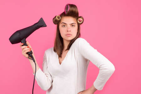 Young funny woman with hair dryer and rollers. Woman with hair dryer. Beautiful girl with straight hair drying hair with professional hairdryer.の写真素材