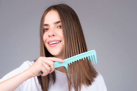 Woman is making hairstyle with comb. Beautiful young woman holding healthy and shiny hair, studio....