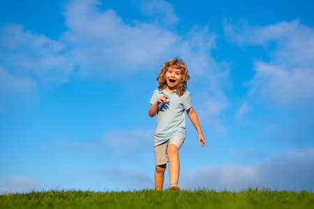 Caucasian boy in a park running and smiling. Happy kid laughing. Emotion face joy child. Joyful, funny spring, summer day, outdoors. Sky background, banner with copy space.の写真素材