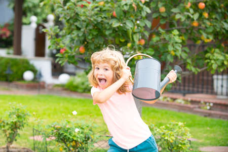 Funny excited kid boy watering flowers and helps to care for the plants with a watering can.