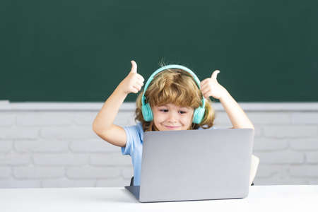 School kids with thumbs up using laptop computer and headphones in class at school.