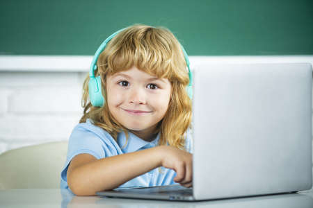 Funny school kid boy with laptop computer and headphones in class at school.