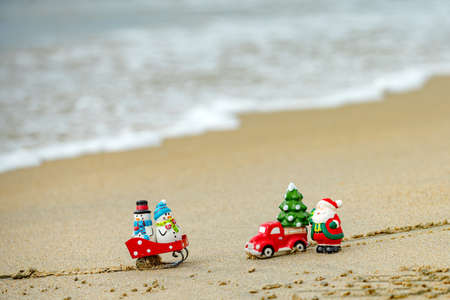 Christmas background. Toy Santa and snowman on summer beach, concept for travel in hot countries.の写真素材