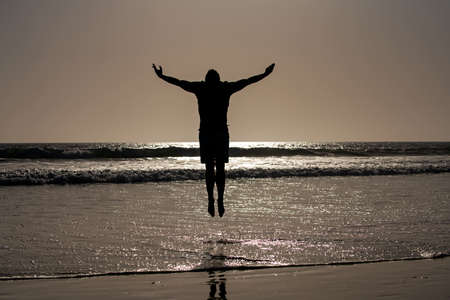 Silhouette of man jumping on beach. Amazing view on sunset beach.