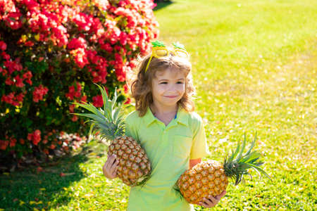 Little blonde kid hugging pineapple on nature background. Childhood, healthy nutrition, advertising. Close up kids funny face, copy space.の写真素材