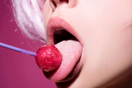 Licking candy. Lollipop model. Woman lips sucking a candy. Glamor sensual model with red lips eat sweats lolly pop.の写真素材