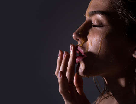 Beautiful woman with honey flows down on her face. Portrait of girl with a honey facialmask closeup. Beautiful woman with honey on her face. Healthy perfect skin. Honey treatment.の写真素材