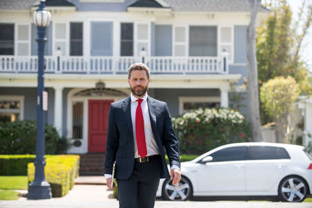 Real estate agent welcoming visitors near new house. Portrait of realtor man.の写真素材