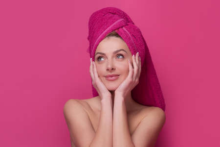 Cosmetic cream on woman face with clean soft skin. Body care. Woman with pink towel applying cream on skin. Body care and spa salon concept. Spa girl. Beautiful young woman with perfect skin.の写真素材