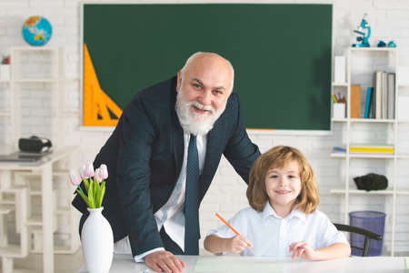 Old senior teacher and young student or school boy. Pupil learning to read and write with teacher in...