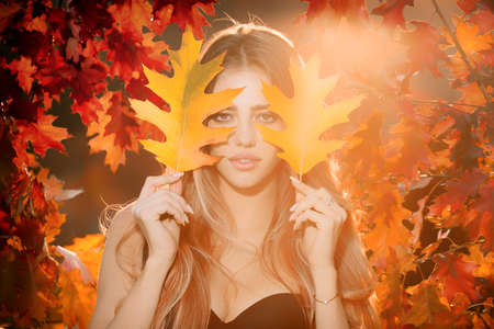 Sensual woman holding autumn leafs in the nature. Beautiful girl enjoying autumn.