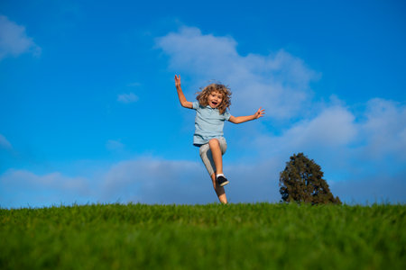 Little adorable boy running on grass. Excited kid play the green grass. The child has blond long hair and a t-shit. The concept of harmony with nature and care for ecology. Healthy lifestyle.の写真素材