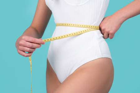 Attractive caucasian woman measuring her waist isolated background. Trained belly with measuring tape.の写真素材