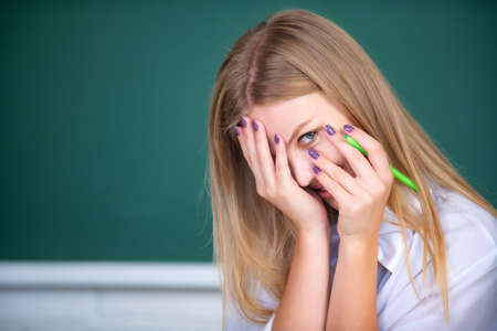 Portrait of young female college shame embarrassed student classroom on class with blackboard background.の写真素材
