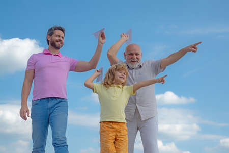 Grandfather father and son playing with paper plane outdoors on sky. Happy family. Three men generation. Happy childhood.の写真素材