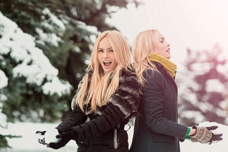 Twins women playing snowballs in forest on snow park. Girls with smiling outdoors on winter day. Christmas and new year girls concept. Active winter lifestyle and vacationの写真素材
