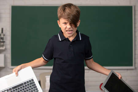 Angry boy in opposition distance education. School kid broken online laptop. Smashing damaged...