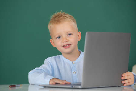 Child boy using a laptop computer at school. Cute pupil face closeup on blackboard background.の写真素材