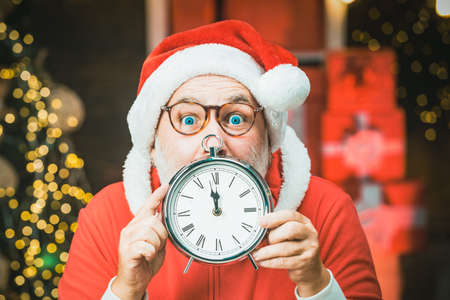 Excited santa holding clock. Photo of Santa pointing at clock showing five minutes to midnight.の写真素材