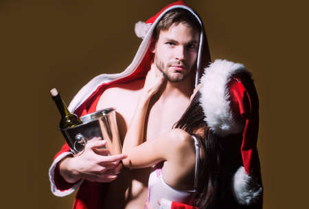 Sexy couple of woman in corset and red christmas hugging muscular man in santa coatの写真素材