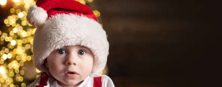 Cute baby face in Santa hat near Christmas tree. Happy Childhood, child 1 year old. New year kids....