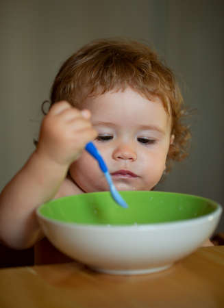 Portrait of funny little baby boy eating from plate holding spoon closeup.の写真素材