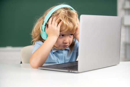 Angry sad boy in headphones sit at desk, study online on laptop at school, klever kid wear earphones in notebook learning using internet lessons.の写真素材