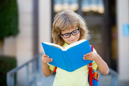 Smiling little student boy wearing school backpack and holding exercise book. Portrait of happy pupil outside the primary school. Closeup face of smiling hispanic schoolkid looking at camera.の写真素材
