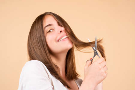 Happy woman with scissors having hair cut. Beautiful girl with straight hair with professional scissor, isolated. Haircare concept.の写真素材