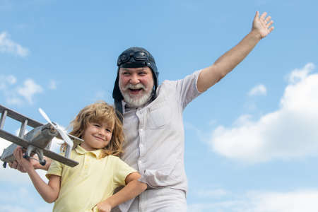 Grandfather and grandson playing with toy plane against summer sky background.の写真素材
