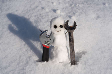 Snow man. Funny snowman on a snowy meadow on a snow background. Wrench and screwdriver. Support repair and service.の写真素材