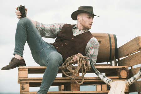 Cowboy on ranch. Handsome man in cowboy hat and retro vintage outfit. Guy drinking whiskey.の写真素材
