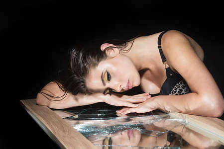 Girl with broken mirror. Elegant young woman posing over black background. Light and shadow. Portrait of a beauty woman face.の写真素材