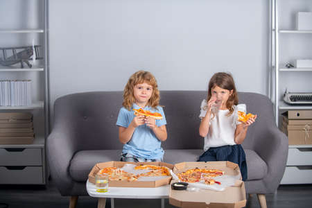 Funny kids eating pizza. Two young children bite pizza indoors.の写真素材