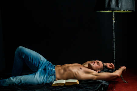 Muscular sleeping sexy guy, lying in bed on black background, naked torso.の写真素材