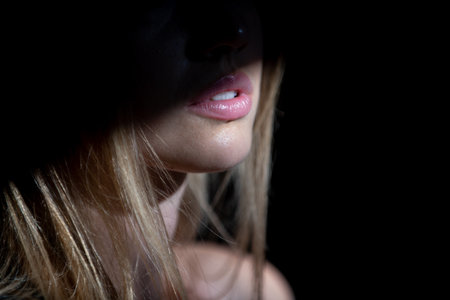 Young woman posing at studio over black background. Light and shadow on lips. Fashion portrait of...