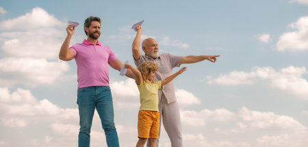 Three different generations ages grandfather father and child son playing with toy plane outdoors.