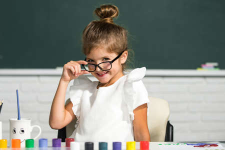 Cute school girl face with glasses. Little girls drawing a colorful pictures with pencil crayons in...