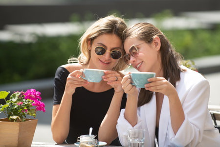 Girl friends in cafe outdoor. Outdoors portrait of two young beautiful women friends drinking coffee.の写真素材