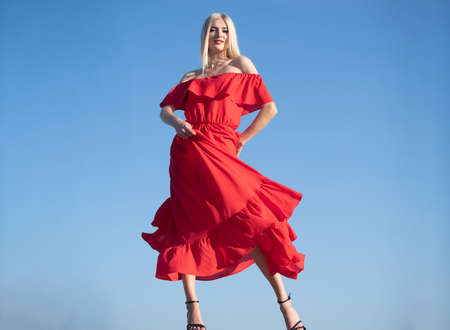 Woman in red dress movement on sky. Beautiful young woman in fashion dress outdoor. Sexy and sensual female model.の写真素材