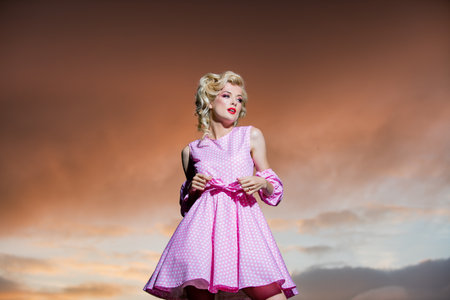 Pinup style woman in summer dress on dramatic sky. Stylish fashion woman posing outdoor. Attractive young woman in sexy dress enjoying summer.の写真素材