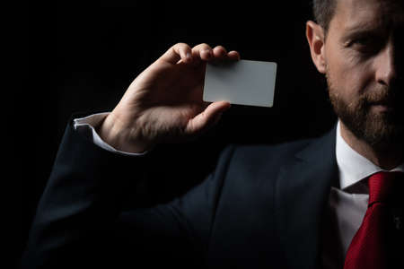 Businessman in black costume and red necktie show credit card or visiting card, close up. Hand holding blank credit card mockup. Creditcard mock up template holding arm.の写真素材