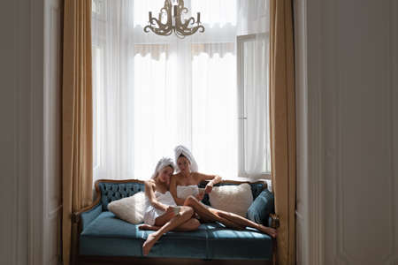 Young sensual women friends relaxing at home. Cozy lazy mornig. Beautiful girls friends in the mornig after sleep on bed. Relaxing female models on the bed.の写真素材