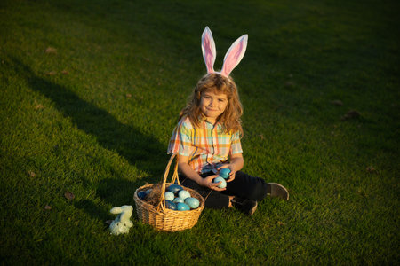 Cute bunny child with rabbit ears. Child boy hunting easter eggs in spring lawn laying on grass.